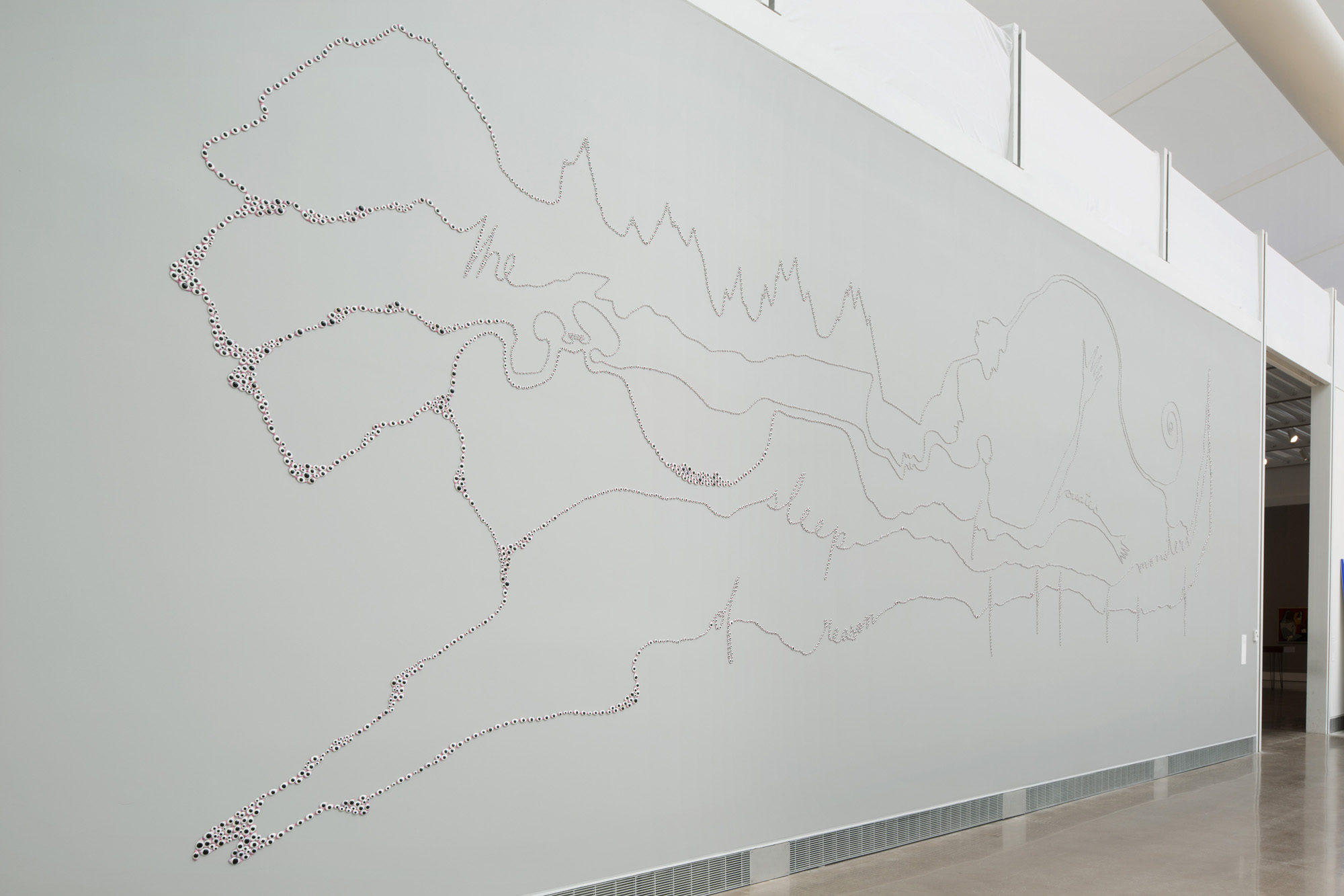 A white exhibition wall with an illustration of an abstract landscape made completely out of tiny eyes. If you look closely at the line work you see the sentence “The sleep of reason creates monsters”.