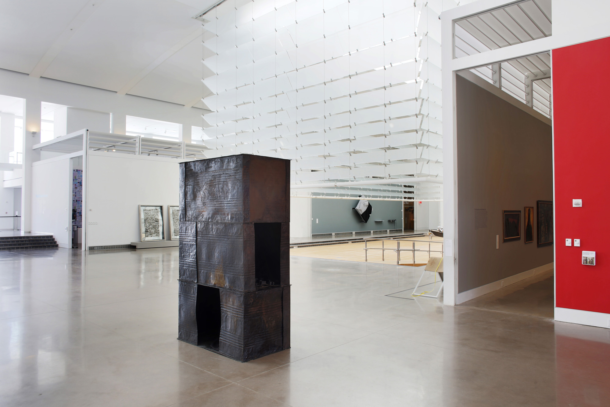 A rectangular-prism shaped sculpture made out of tar drum sheets, installed on an empty exhibition floor. In the background are entryways to other exhibition spaces.