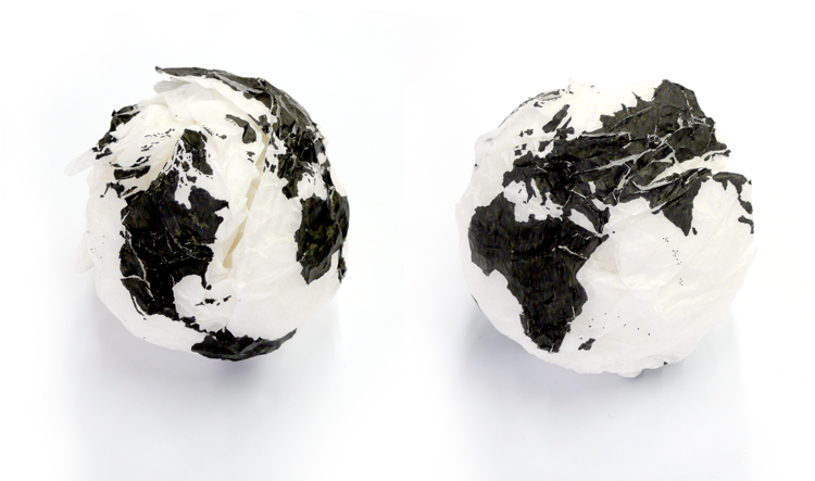 Against a white backdrop, two white, clumped up, paper balls are placed side by side. Drawn across the two of them is a black, ink drawing of the world map.