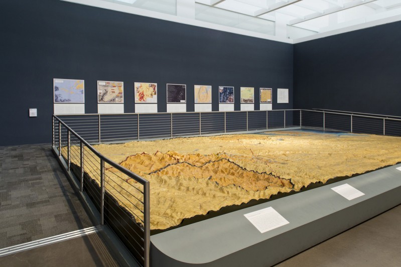 A large-scale relief map of New York City’s watershed, installed in an exhibition space with navy blue walls. The relief map is guarded off by a metal railing on three sides. Along the longest exhibition wall are eight maps accompanied by wall text.