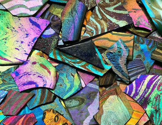 A close up view of iridescent shards of glass. The shards of glass are in different colors and patterns. Some have stripes, some of swirls and some have spots. Each piece has a glow or sheen to it.
