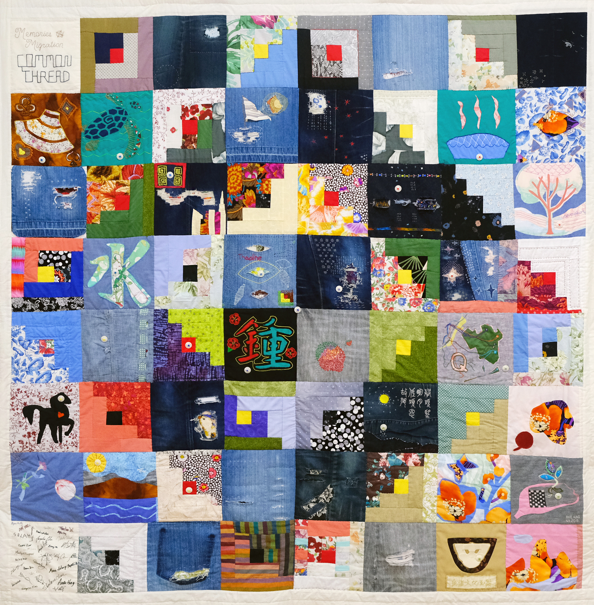 A square quilt made up of 64 smaller squares patches and a thin white perimeter. The first square, on the top left, has the words “Memories Migration Common Thread” embroidered on a white patch with black thread. Each of the other patches are made up of different colors with either abstract shapes, letters, or motifs.