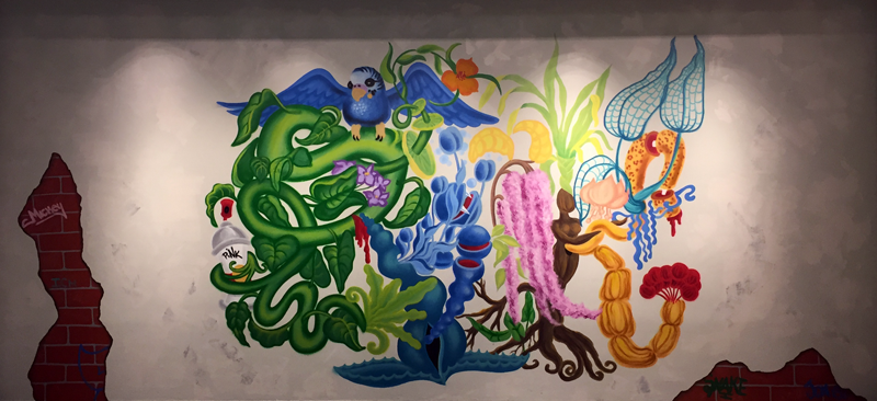 Graffiti art, of stylized green vegetation, different colored flowers, and a blue bird against a white wall. The wall is torn on the edges, revealing a brick wall underneath.
