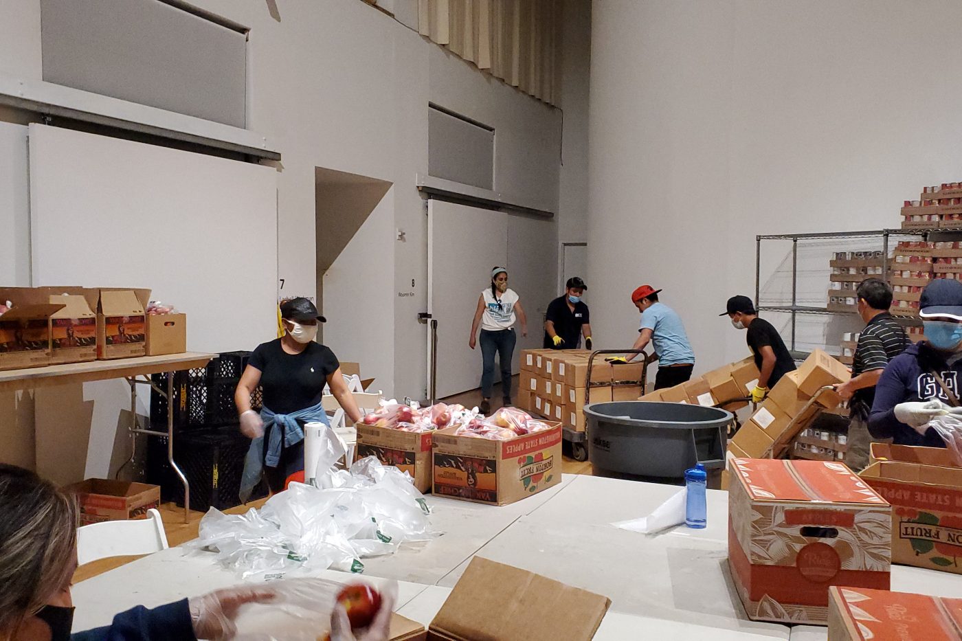 Seven Cultural Food Pantry Volunteers are moving, boxing, and unboxing fresh produce and canned goods inside the Queens Museum.