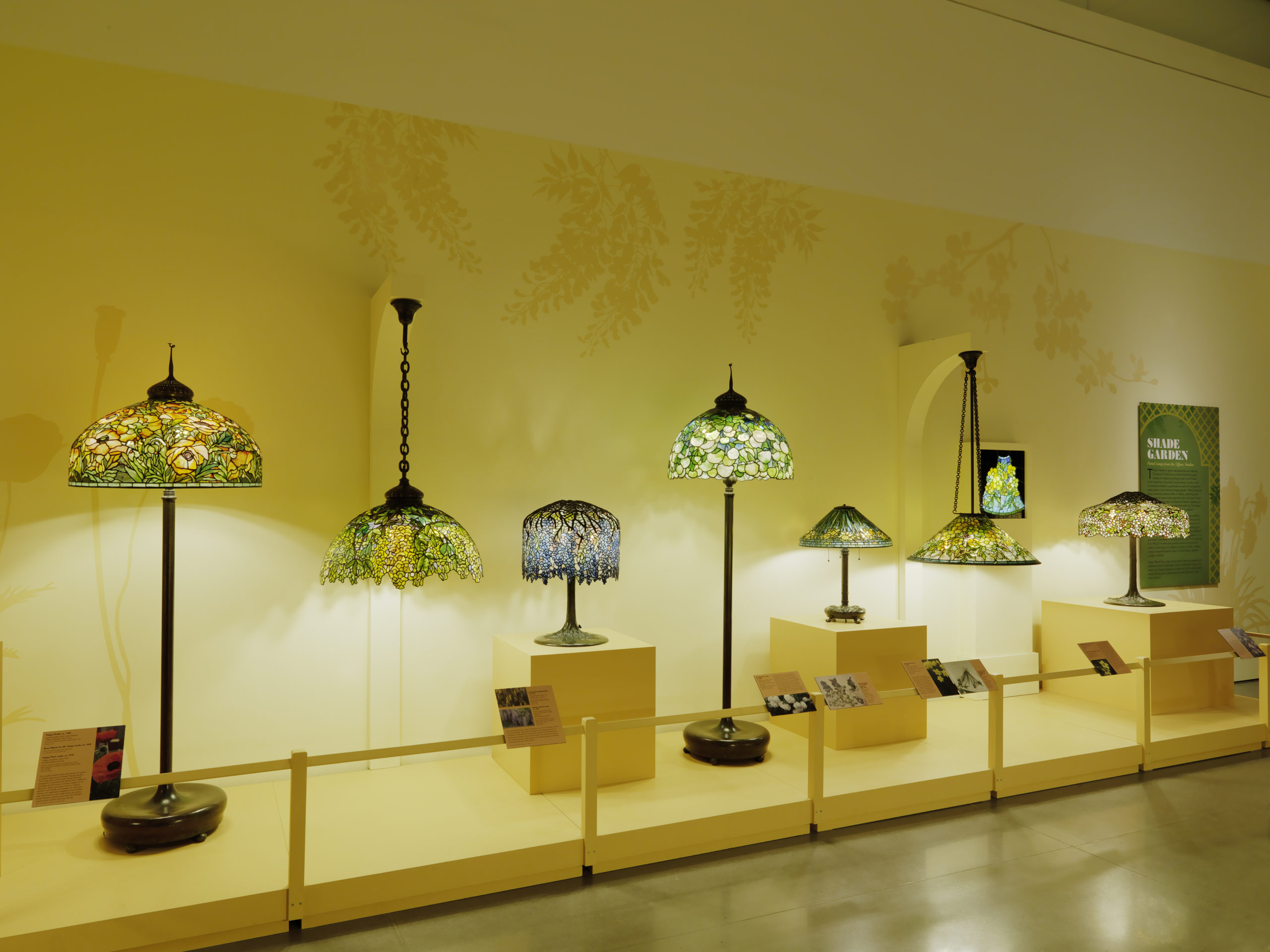 Step into a room of “ richly colored glass and sculpted bronze” Tiffany lamps with varying designs including daffodil and dragonflies. Six tall standing lamps greet you at the door with their original prices listed . Around the gallery are smaller desk lamps. The room includes video demonstrations of how to make glass and colorful glass pieces in glass cases.