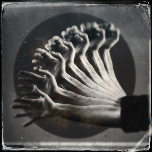 A black and white alternative process photograph showing the traces of an arm and hand as it moves from the hand position of a fist to an open palm.