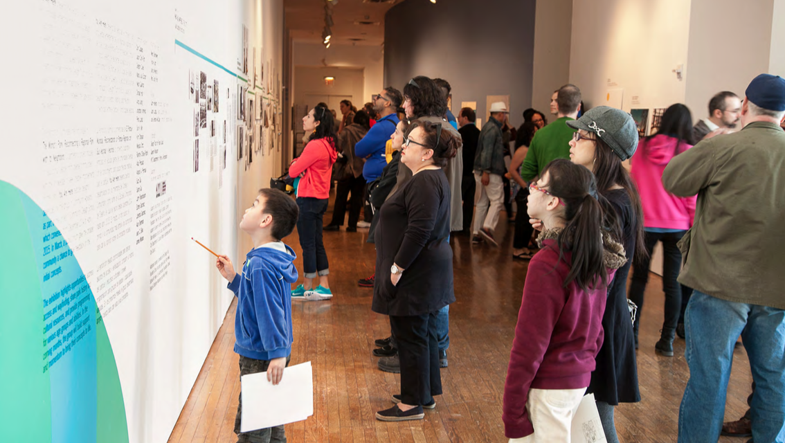 A group of visitors of different ages, genders, and races looking at an exhibition wall on the Museum's second floor with didactic material about The World's Park program.