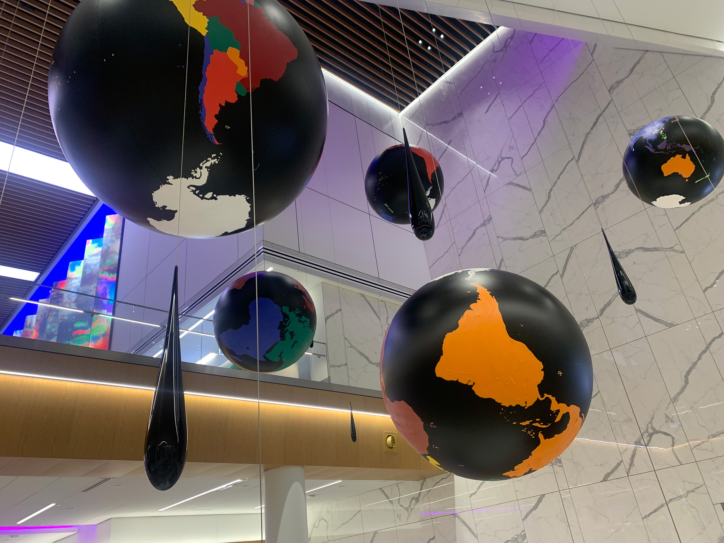 A video thumbnail with a centered, black “press play” symbol in a green rounded off square. The thumbnail is of four black starlight globes in different orientations and black droplets hanging from a museum ceiling.