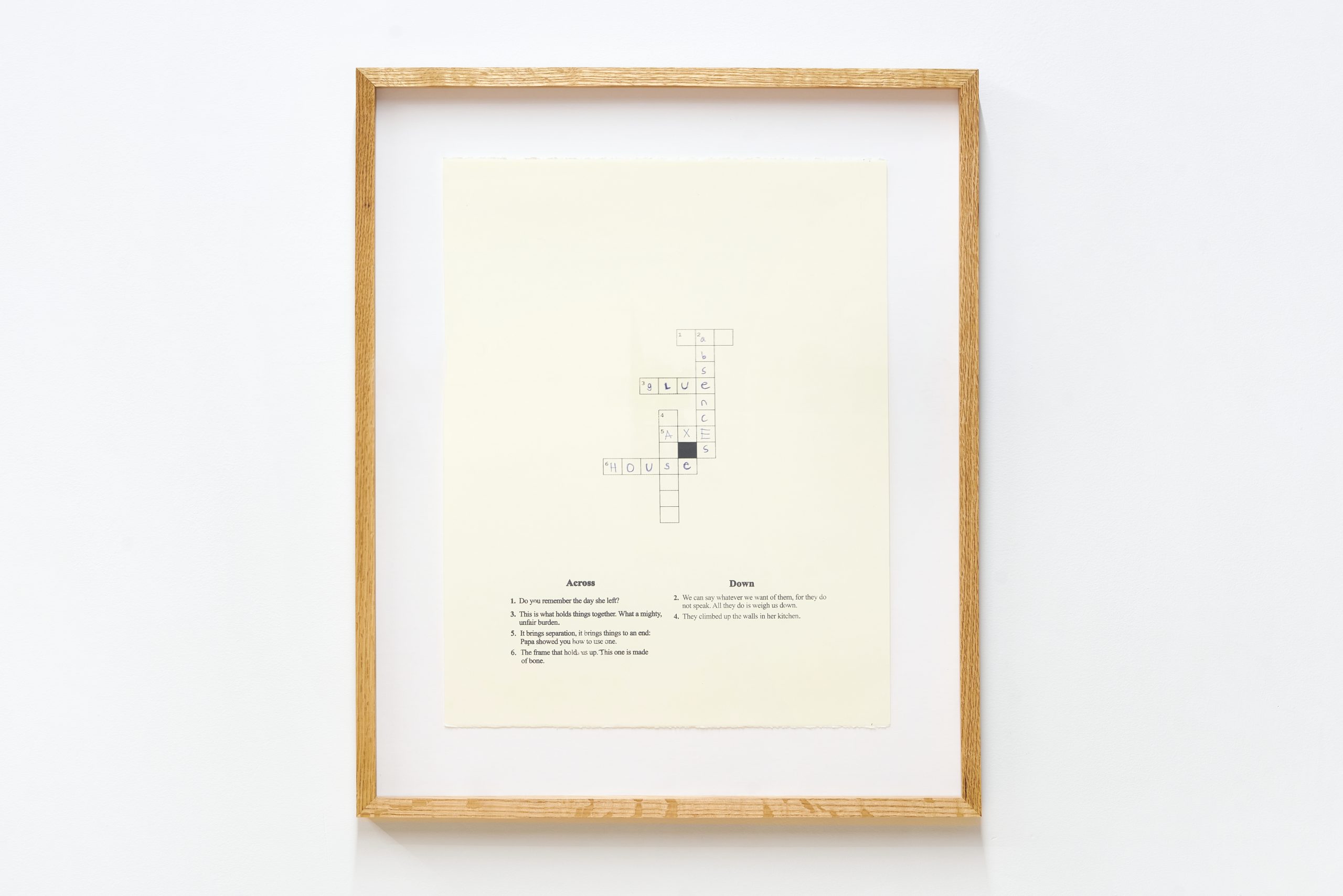 a crossword puzzle printed on a cream colored piece of paper in a wooden frame on a white wall